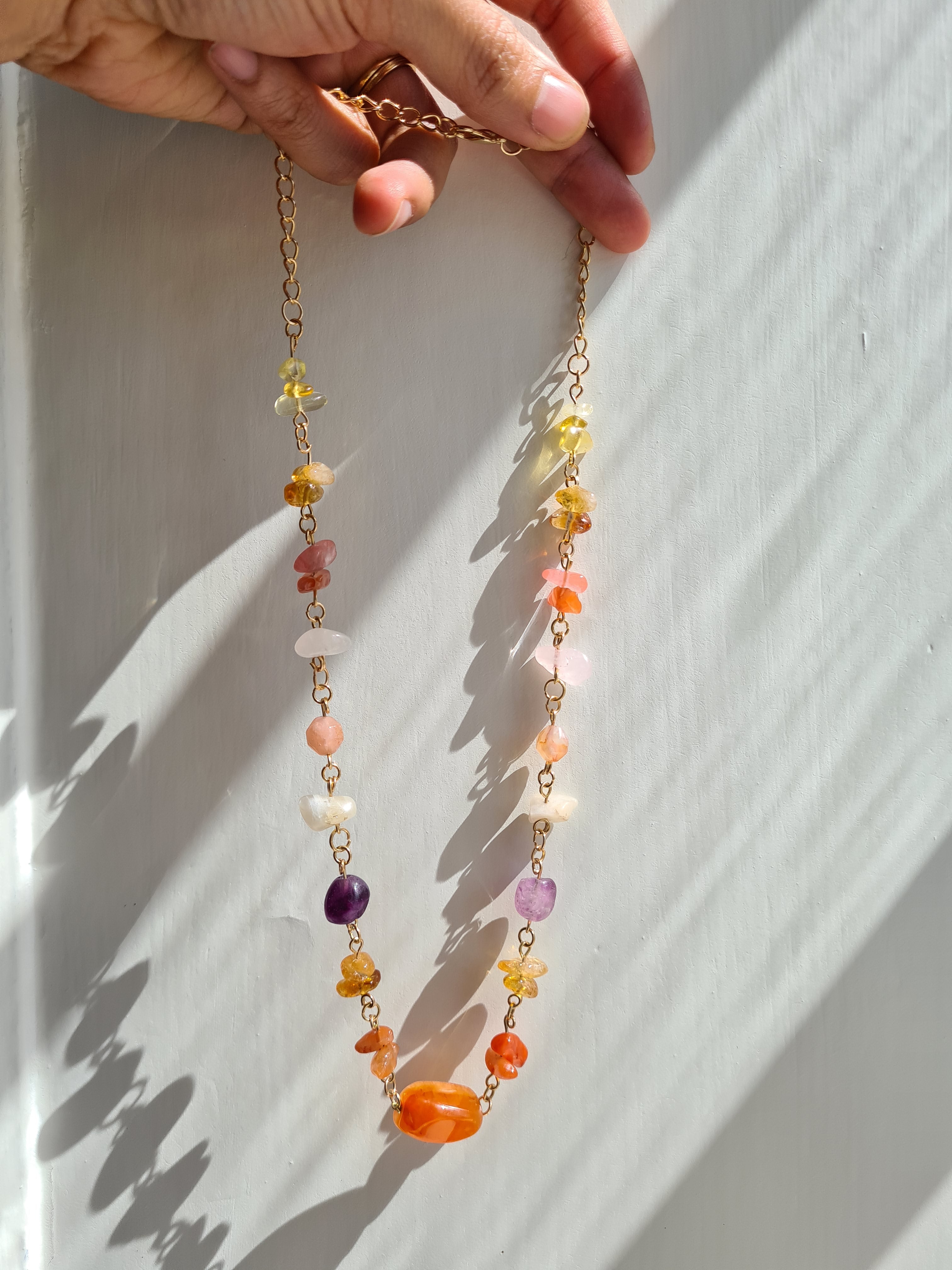 Mixed gemstone necklace held up in sunlight